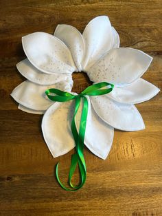 a white flower with green ribbon tied around it on a wooden table next to a pair of scissors