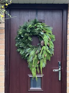 a wreath is hanging on the front door of a house with pine cones and greenery