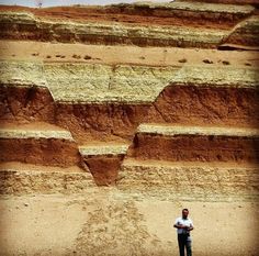 a man standing in front of a large formation of rocks and sand with the shape of a heart drawn on it