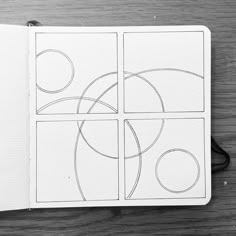 an open notebook with some lines drawn on the pages and circles in each section, sitting on top of a wooden table