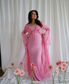 a woman in a pink dress standing next to flowers and wearing a long shawl