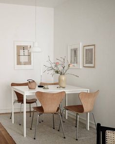 a white table with four chairs and a vase on it in a room filled with pictures