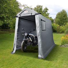 a motorcycle is parked in front of a tent on the grass near some trees and bushes