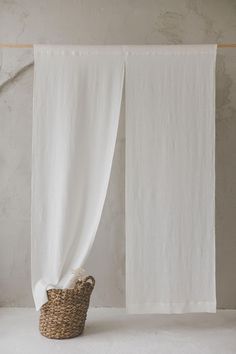 a white curtain with a basket in front of it on top of a floor next to a wall