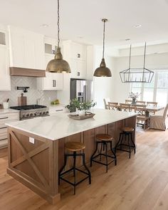 a large kitchen island with stools in it and two pendant lights hanging from the ceiling