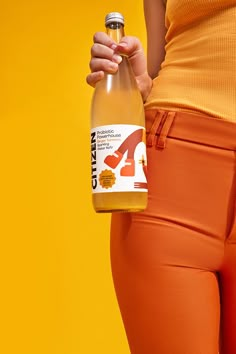 a woman holding a bottle of orange juice in her right hand while standing against an orange background