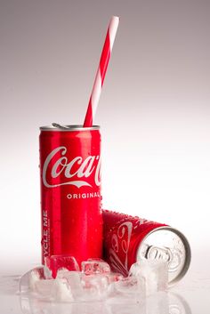 a can of coca - cola sitting on top of ice with a straw in it