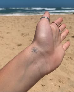 a person's hand with a small tattoo on it, in front of the ocean