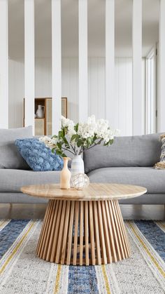 a living room with a gray couch and white flowers on the coffee table in front of it