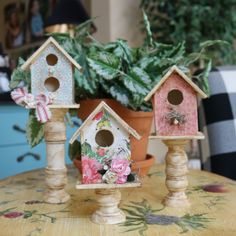 three bird houses sitting on top of a table next to a potted plant with pink flowers