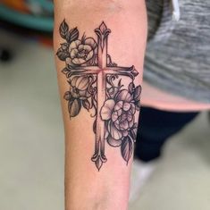 a cross with flowers and leaves on the arm is shown in this tattoo style photo