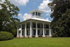 a large white house sitting in the middle of a lush green field next to trees