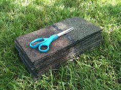 a pair of blue scissors sitting on top of a piece of black rock in the grass