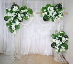 an arrangement of flowers and greenery in front of a white drapeed backdrop