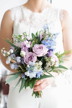 a bride holding a bouquet of purple and blue flowers on her wedding day in front of a mirror