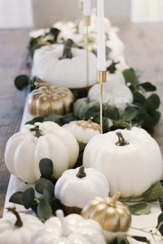 white pumpkins and greenery are arranged on a long table with gold candlesticks