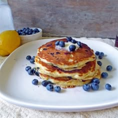 three pancakes with blueberries and syrup on a white plate next to two lemons