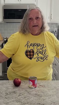 an older woman with grey hair wearing a happy rabies t - shirt standing at a kitchen counter