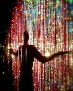 a man is standing in front of a curtain with lights on it and his arms out