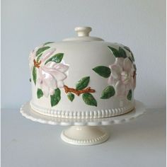 a white cake with pink flowers and green leaves painted on the top is sitting on a pedestal