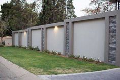 a fenced in area with grass and bushes next to the wall that has lights on it