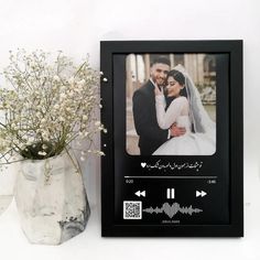 a black frame with an image of a bride and groom on it next to a vase filled with baby's breath flowers