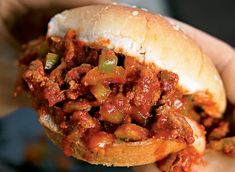 a hand holding a sandwich filled with meat and sauce on top of it's bun