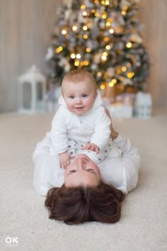 a woman holding a baby in front of a christmas tree