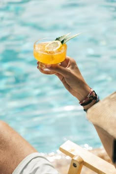 a person holding up a drink in front of a swimming pool