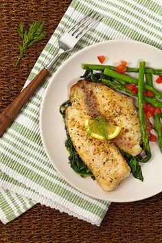 two fish fillets with asparagus and tomatoes on a plate next to a fork