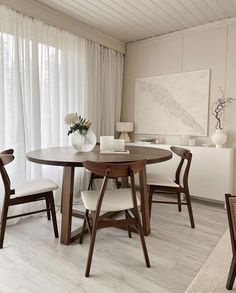 a dining room table with four chairs and a vase on top of it in front of a window