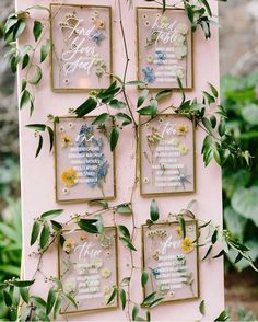 a pink and gold wedding seating chart with greenery on the sides, hanging from a wall