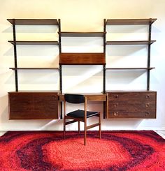 a room with a rug, chair and shelving unit on the wall next to it