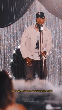 a man standing in front of a microphone on top of a stage next to a curtain