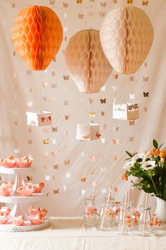 three paper lanterns hanging from the ceiling above a table with flowers and cake on it