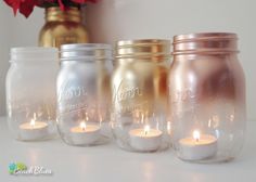 four mason jars with candles in them sitting on a table next to a red flower