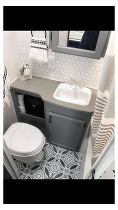 a white toilet sitting next to a sink in a bathroom under a window on top of a tiled floor