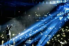 a man standing on top of a stage with his arms in the air and lights behind him