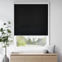 a black roller blind in a white room with a plant on the window sill