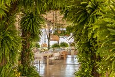 the inside of a restaurant with tables and chairs surrounded by greenery on either side