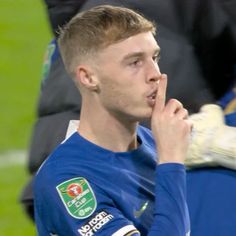 a young man in a blue shirt is holding his hand to his mouth while standing on the field