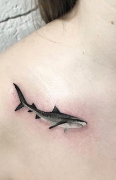 a black and white photo of a shark tattoo on the back of a woman's shoulder