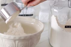 a person pouring flour into a white bowl