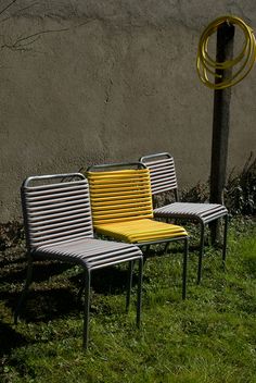 two chairs sitting next to each other in the grass near a wall with a spiral design on it