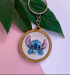 the stitcher keychain is hanging from a green leafy branch, which has been placed on a pink and white background