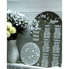 a table seating sign next to a vase with flowers