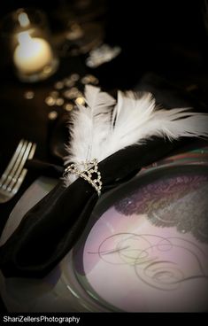 a plate with a feather on it next to a candle and some silverware in the background