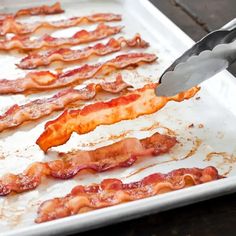 bacon being cooked on a baking sheet with a spatula