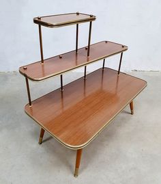 three tiered wooden shelf with glass shelves on the top and bottom, against a white wall