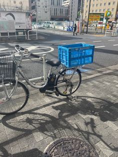 a bicycle parked next to a blue basket on the side of a street with buildings in the background